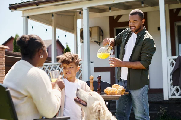 Joyeux afro-américain garçon souriant et debout près du chien et des parents pendant le barbecue familial sur la cour — Photo de stock