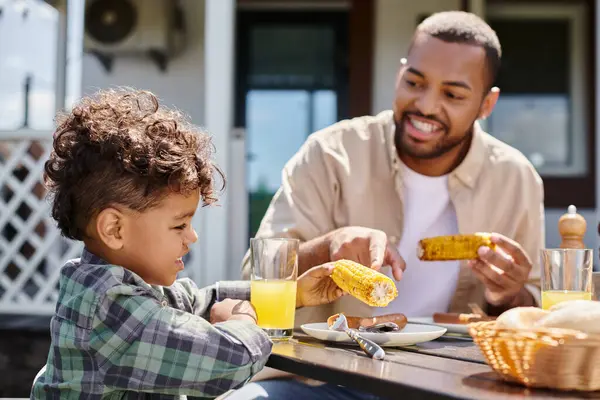 Positivo africano americano niño tener familia barbacoa con padre en patio trasero de la casa, zumo de naranja - foto de stock