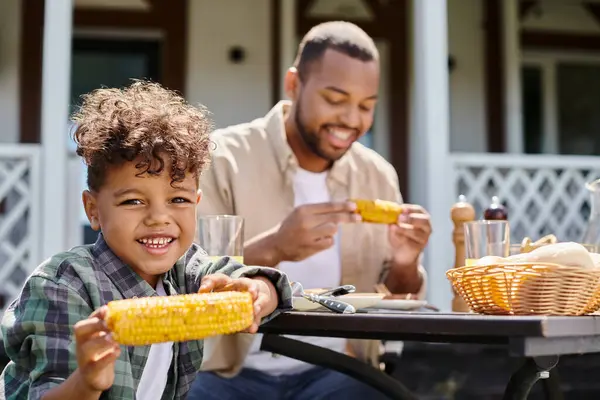 Alegre africano americano niño tener familia barbacoa con padre en patio trasero de la casa, jugo de naranja - foto de stock