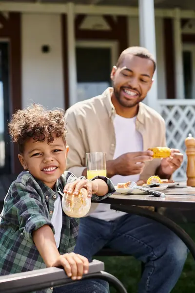 Alegre africano americano niño tener familia barbacoa con padre en patio trasero de casa, celebración de moño - foto de stock
