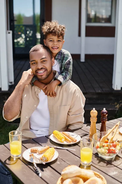 Heureux afro-américain enfant étreignant père tout en ayant barbecue sur la cour de la maison, famille — Photo de stock