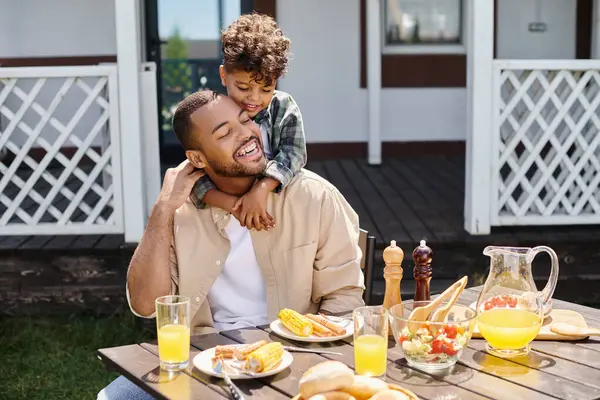 Positif afro-américain enfant étreignant père tout en ayant barbecue sur la cour de la maison, famille — Photo de stock