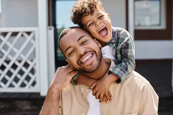 Positivo afroamericano ragazzo abbracciare padre eccitato in bretelle sul cortile di casa, tempo di qualità — Foto stock