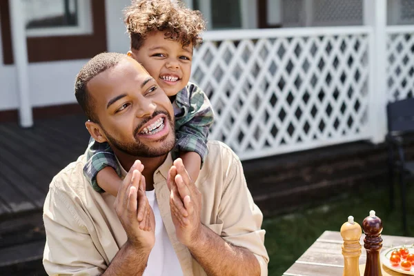 Positivo afro-americano menino abraçando animado pai em aparelho no quintal da casa, tempo de família — Fotografia de Stock