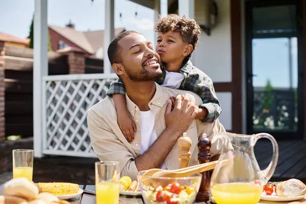 Bonito afro-americano criança abraçando animado pai no aparelho no quintal da casa, tempo de família — Fotografia de Stock
