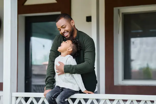 Fröhliche afrikanisch-amerikanische Junge sitzt auf Veranda und umarmt mit Vater in Zahnspange auf Hinterhof — Stockfoto