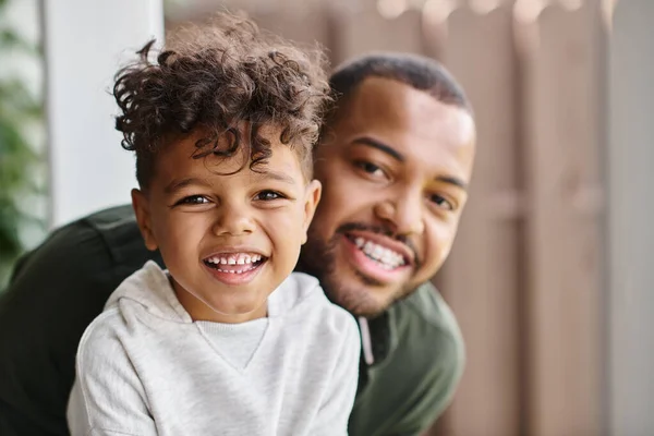 Сімейний портрет веселого афроамериканця в брекетах, що обіймають кучерявого сина, дивлячись на камеру — стокове фото