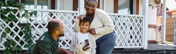 Familienbanner, fröhliche afrikanisch-amerikanische Eltern und Sohn lächeln neben niedlichem Hund im Hinterhof des Hauses — Stockfoto