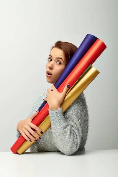 Surprised woman with short hair holding colorful wrapping paper on grey backdrop, Christmas concept — Stock Photo