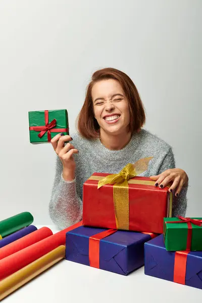 Femme heureuse en pull d'hiver près enveloppé cadeau de Noël et papier cadeau coloré sur gris — Photo de stock