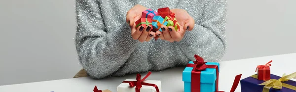 Banner einer beschnittenen Frau mit einem Strauß winziger Weihnachtsgeschenke in der Nähe bunt verpackter Geschenke auf grau — Stockfoto