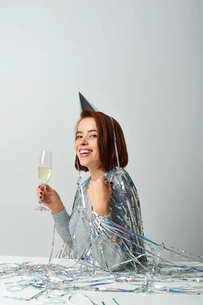 Mujer alegre en gorra de fiesta con oropel en la cabeza sosteniendo una copa de champán mientras celebra la Navidad - foto de stock