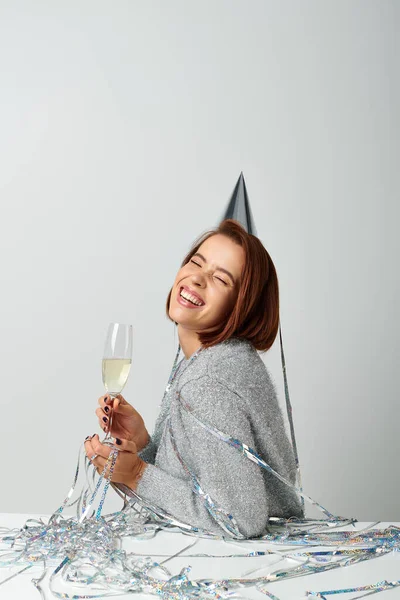 Cheerful woman in party cap and tinsel on head holding champagne glass while celebrating New year — Stock Photo