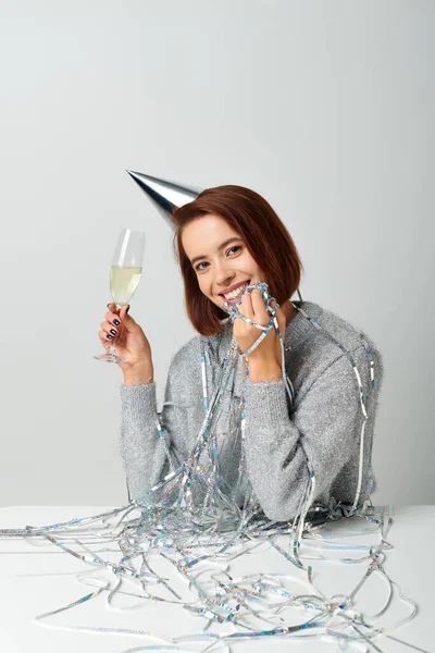 Задоволена жінка в партійній шапці і мішурі на голові тримає келих шампанського під час святкування Нового року — стокове фото