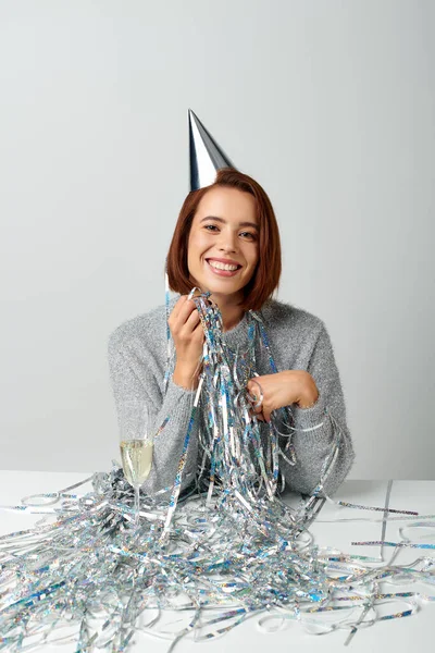 Donna contenta in berretto partito e fili di lame sorridente vicino bicchiere di champagne durante la celebrazione del nuovo anno — Foto stock