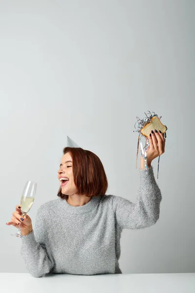 Excited woman in party cap holding champagne glass and sandwich with tinsel, Merry Christmas concept — Stock Photo