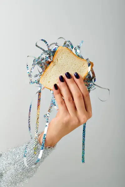 Cropped female hand holding sandwich with shiny tinsel on grey backdrop, Happy New Year concept — Stock Photo