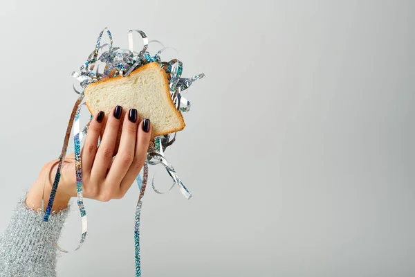 Vue recadrée de femme tenant sandwich avec tinelle brillante sur fond gris, concept Bonne année — Photo de stock