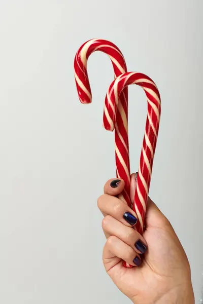 Vista ritagliata della donna che tiene canne di caramelle rosse a spirale su sfondo grigio, concetto di Buon Natale — Foto stock