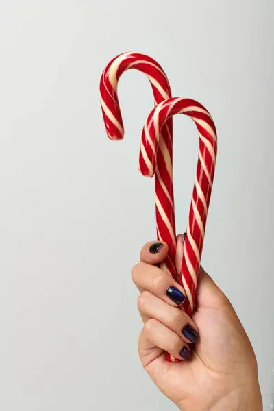 Cropped view of woman holding spiral red candy canes on grey background, Merry Christmas concept — Stock Photo