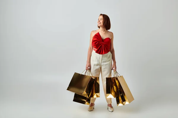 Compras de vacaciones, mujer feliz en traje de moda sosteniendo bolsas de compras sobre fondo gris, Navidad - foto de stock