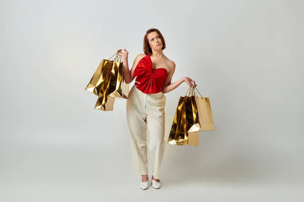 Holiday shopping, confused woman in stylish attire holding shopping bags on grey background — Stock Photo