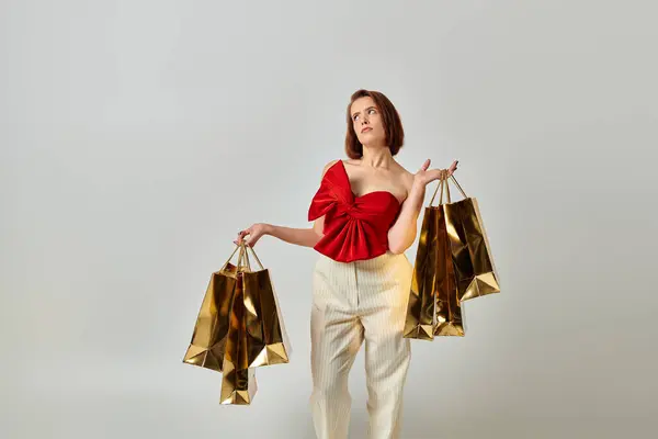 Holiday shopping, pensive woman in stylish attire holding shopping bags on grey background — Stock Photo