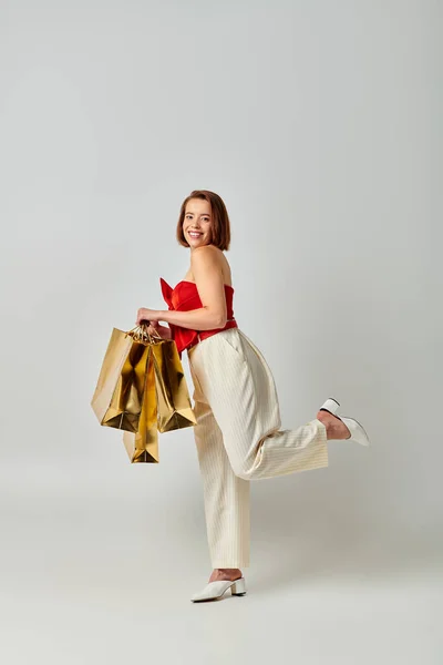 Compras de Natal, jovem mulher feliz em traje na moda segurando sacos de compras em fundo cinza — Fotografia de Stock