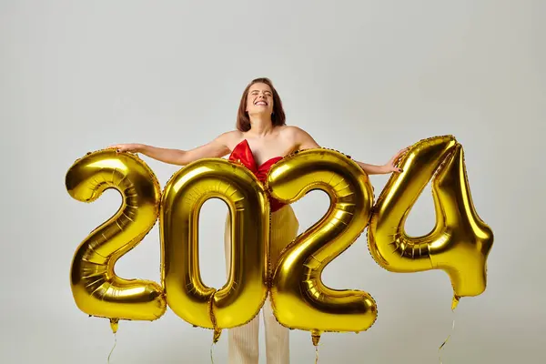 Happy New Year, joyful young woman in trendy attire holding balloons with 2024 numbers on grey — Stock Photo