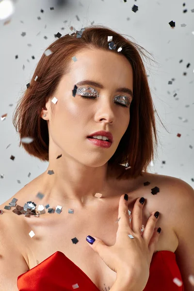 Maquiagem festiva, jovem mulher com cabelo curto e sombra de olhos cintilantes posando com olhos fechados em cinza — Fotografia de Stock
