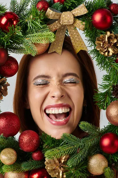 Close up of cheerful woman with shimmery makeup smiling inside frame of decorated Christmas wreath — Stock Photo