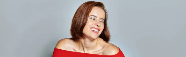 Jovem mulher satisfeita com cabelo curto morena posando em traje vermelho no fundo cinza, banner — Fotografia de Stock