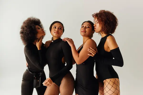 Cuatro mujeres afroamericanas atractivas en traje atractivo negro posando juntas, concepto de moda - foto de stock