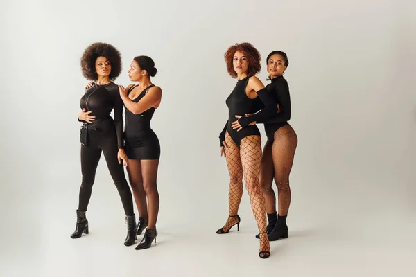 Four appealing african american women in black alluring attire posing together, fashion concept — Stock Photo