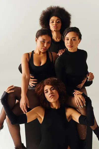 Mujeres afroamericanas atractivas en trajes atractivos negros posando en cubo negro, concepto de moda - foto de stock