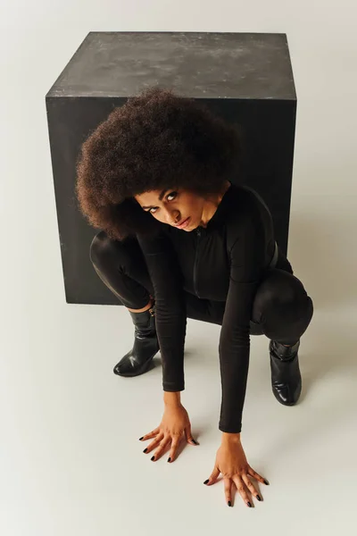Hermosa modelo femenina afroamericana en traje negro posando junto al cubo negro, concepto de moda - foto de stock