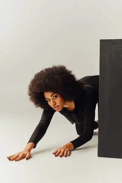 Hermosa modelo femenina afroamericana en traje negro posando junto al cubo negro, concepto de moda - foto de stock