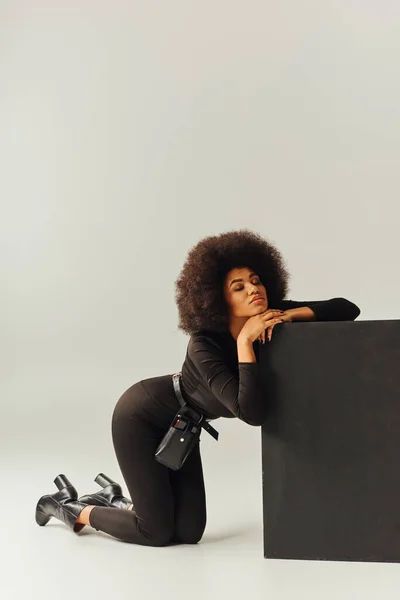 Hermosa modelo femenina afroamericana en traje negro posando junto al cubo negro, concepto de moda — Stock Photo
