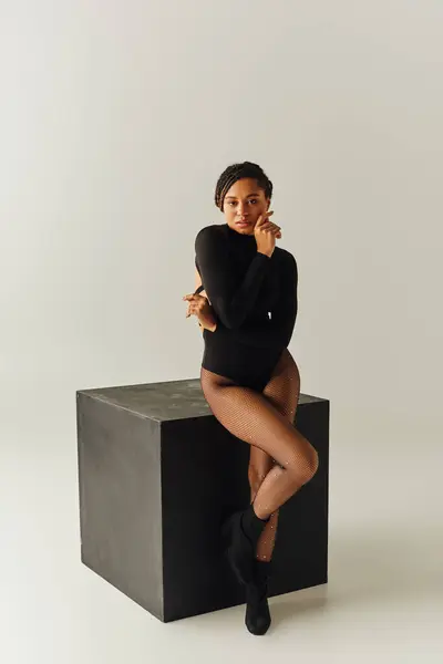 Alluring african american woman in sexy tights and bodysuit posing next to black cube, fashion — Stock Photo