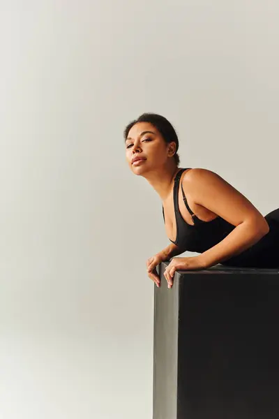 Appealing african american female model in sexy attire lying on black cube, fashion concept — Stock Photo