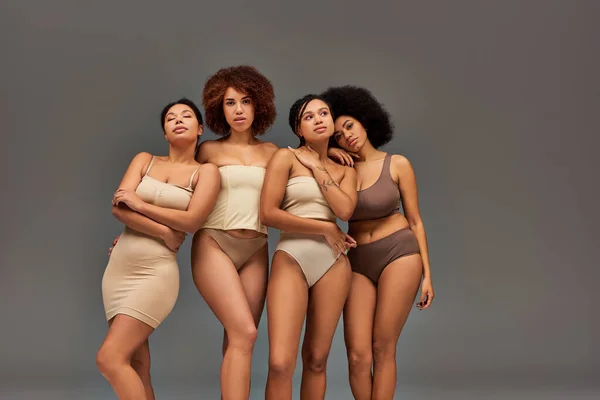 Cuatro mujeres afroamericanas atractivas en ropa interior pastel posando juntas sobre fondo gris, moda - foto de stock