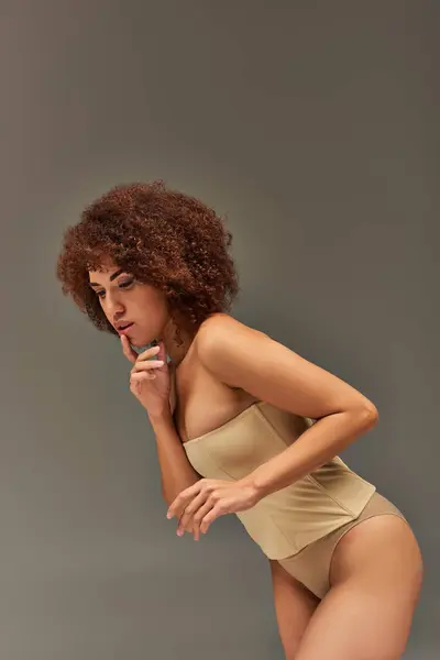 Séduisant modèle féminin afro-américain en sous-vêtements pastel posant sur fond gris, concept de mode — Photo de stock