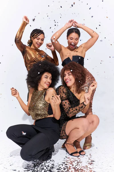 Stylische attraktive afrikanisch-amerikanische Frauen feiern unter Konfettiregen auf dem Boden sitzend, Mode — Stockfoto