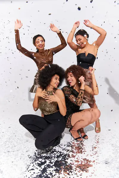 Mujeres afroamericanas atractivas elegantes que festejan bajo la lluvia del confeti que se sienta en piso, moda - foto de stock