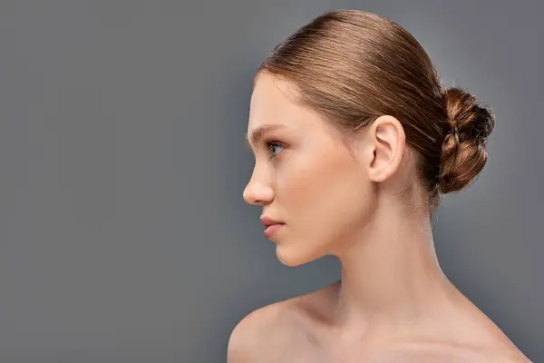Vista lateral da jovem com pele perfeita e ombros nus olhando para o fundo cinza — Fotografia de Stock