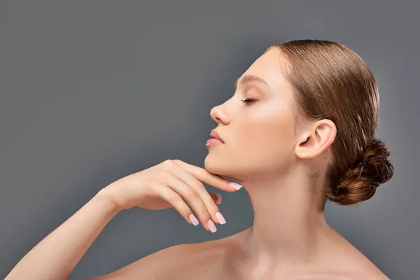 Side view of young woman with perfect skin and bare shoulders posing with hand near chin on grey — Stock Photo