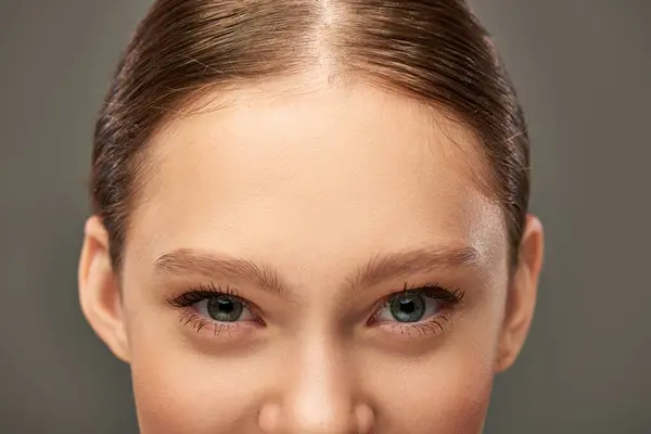 Vista cortada de mulher jovem com olhos azuis e pele perfeita olhando para a câmera no fundo cinza — Fotografia de Stock