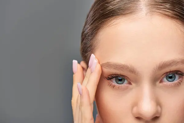 Schnappschuss einer jungen Frau mit blauen Augen und perfekter Haut, die in die Kamera auf grauem Hintergrund blickt — Stockfoto