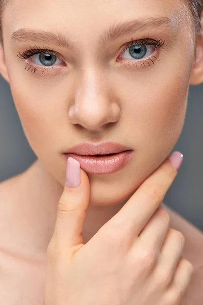 Close up de mulher bonita com olhos azuis e pele perfeita tocando seu rosto no fundo cinza — Fotografia de Stock