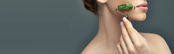 Giovane donna con pelle perfetta massaggio viso con rullo di giada su sfondo grigio, banner per la cura della pelle — Foto stock